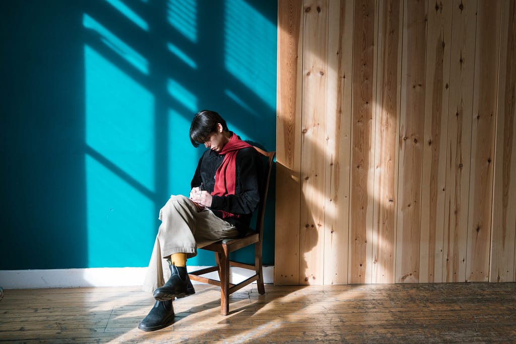 A writer sits writing into a notepad against a blue wall. and suns shines shadows on to him.