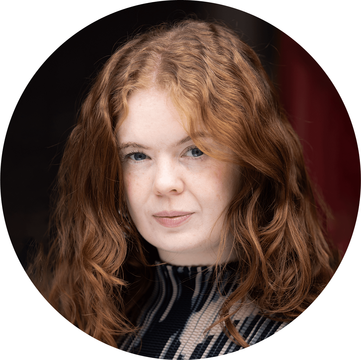A young woman with red hair and a nice patterned jumper stares into the camera