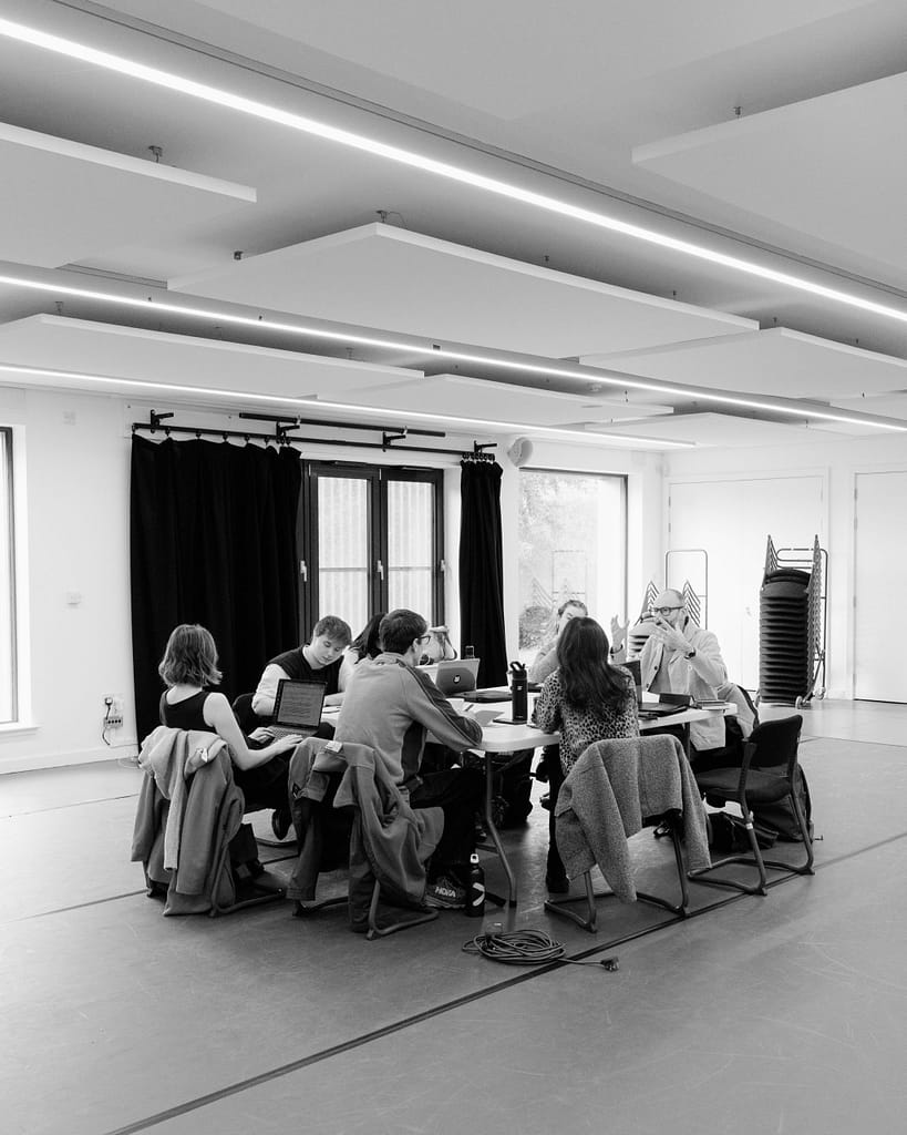 A black and white image with a group of people sitting at a table in the middle of the room.